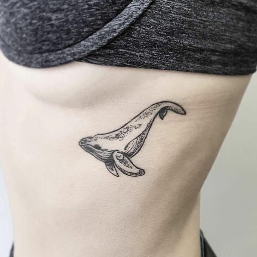 Черная маленькая татуировка на теле девушки в виде кита